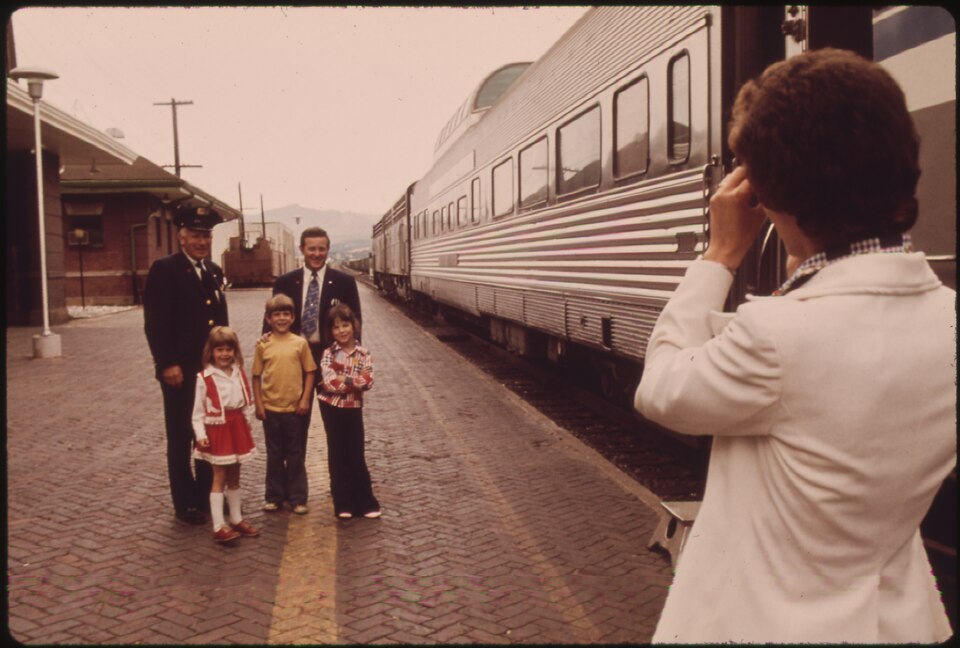 Mom Takes — MOM TAKES A PICTURE OF THE KIDS WITH RAILROAD_PERSONNEL AT THE WENATCHEE, WASHINGTON, DEPOT AS THE EXPO '74 PASSENGER TRAIN MAKES A 10 MINUTE STOP ENROUTE BETWEEN SPOKANE AND SEATTLE AMTRAK REVERSED A 25-YEAR DECLINE IN RIDERSHIP AFTER IT ASSUMED RESPONSIBILITY FOR MOST U.S. INTERCITY RAIL PASSENGER SERVICE IN 1971